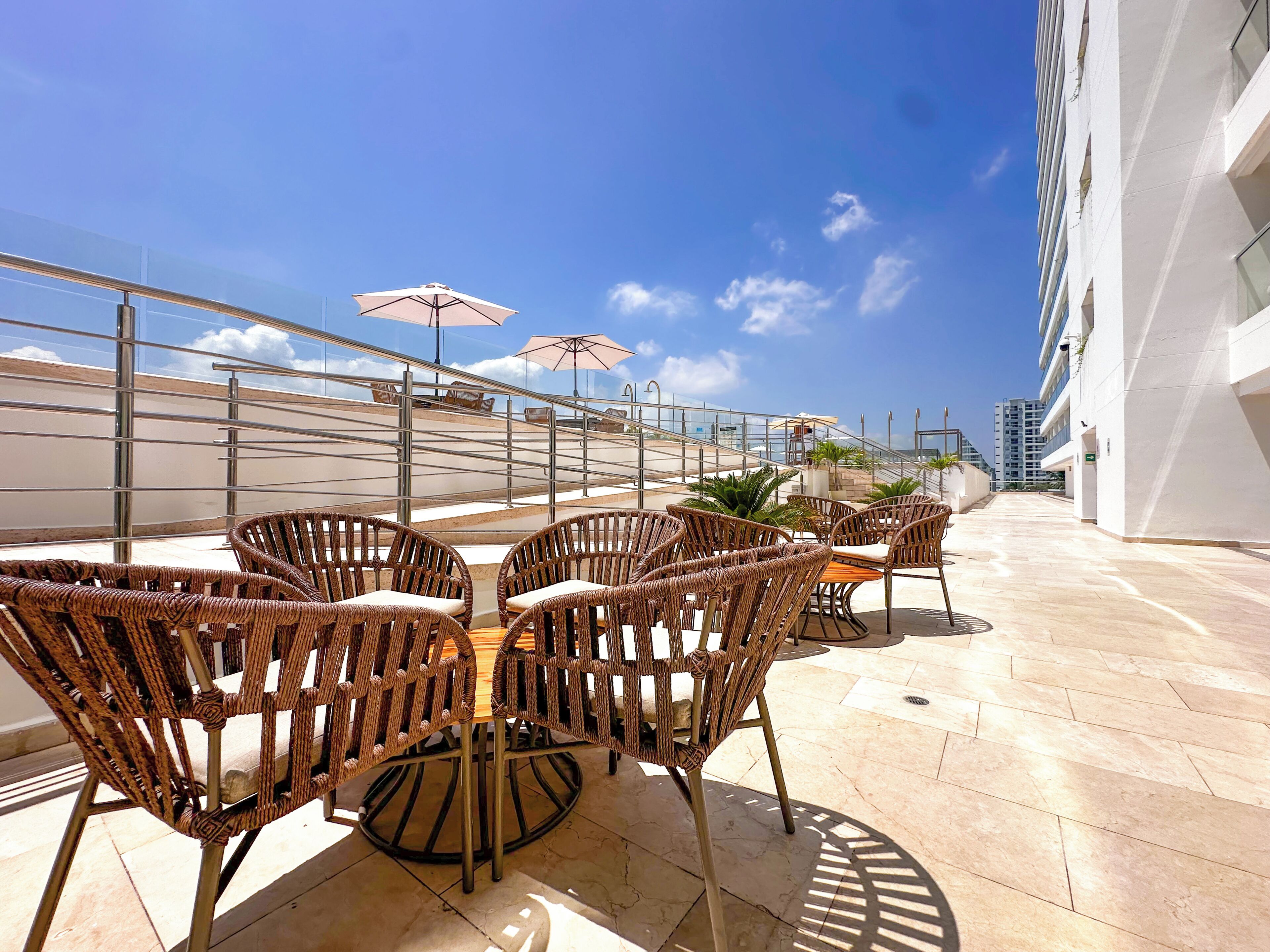 Una terrazza sul tetto con sedie e tavoli in vimini, ombrelloni e vista su un edificio moderno.