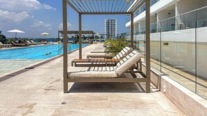 Zona de piscina en la azotea con sillones de descanso, una pérgola y vistas del horizonte urbano.