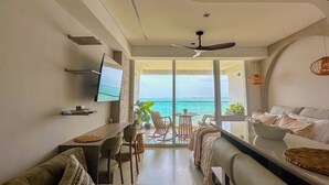 Un salón moderno con sofá, una mesa de comedor y televisor. Hay un balcón con vistas al mar.