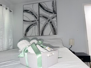 A hotel room with a bed, a basket of toiletries, and abstract wall art. - Relaxing Douglasville Home Near Arbor Place Mall, with WiFi Perfect for Families (Douglasville)