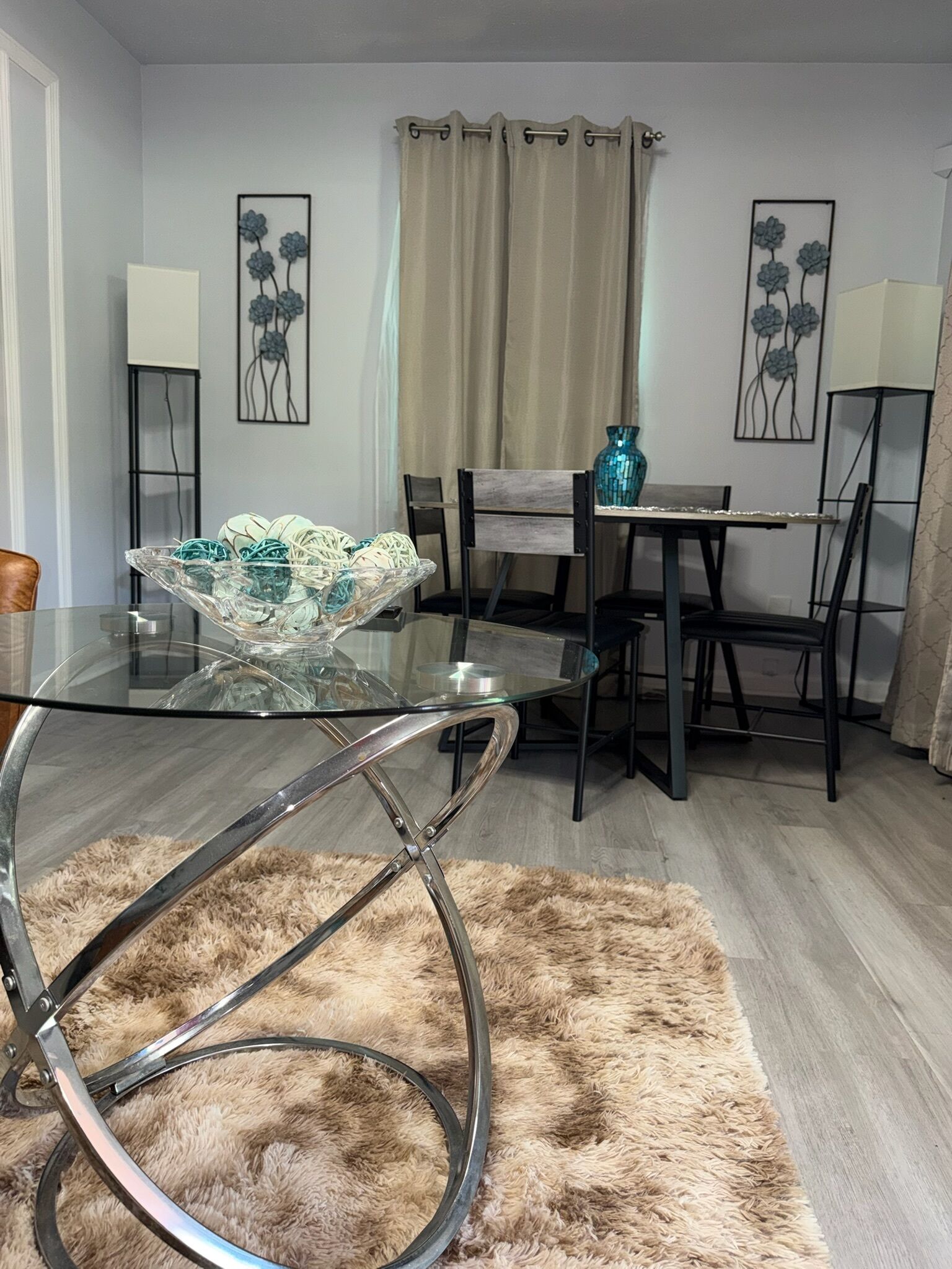 Un comedor moderno con una mesa de vidrio, sillas de metal, un tapete mullido y decoración en la pared.