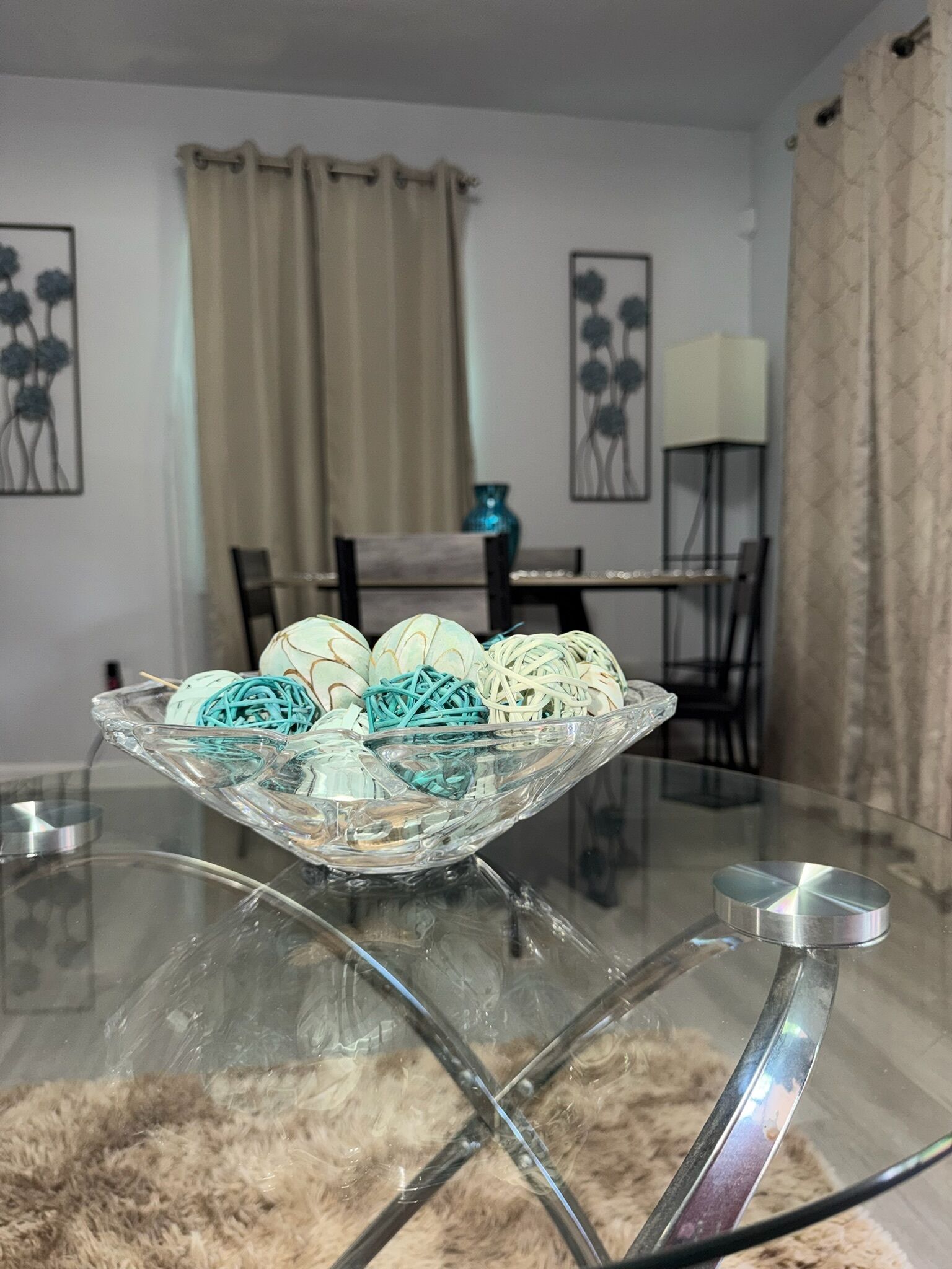 Una mesa de vidrio con un cuenco decorativo que contiene bolas de colores y una alfombra mullida.