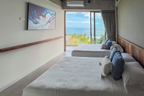 A hotel room with two beds, a large window with a view of the ocean, and a painting on the wall. - View and Surf: Modern 2-Bedroom Apartment in El Zonte (La Libertad Costa)