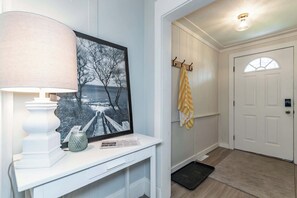 Ein Flur mit einer weißen Tür, einem Kleiderständer mit einem gelben Handtuch, einem gerahmten Bild, einer Lampe und einem kleinen Tisch mit einer Vase und einer Zeitung.