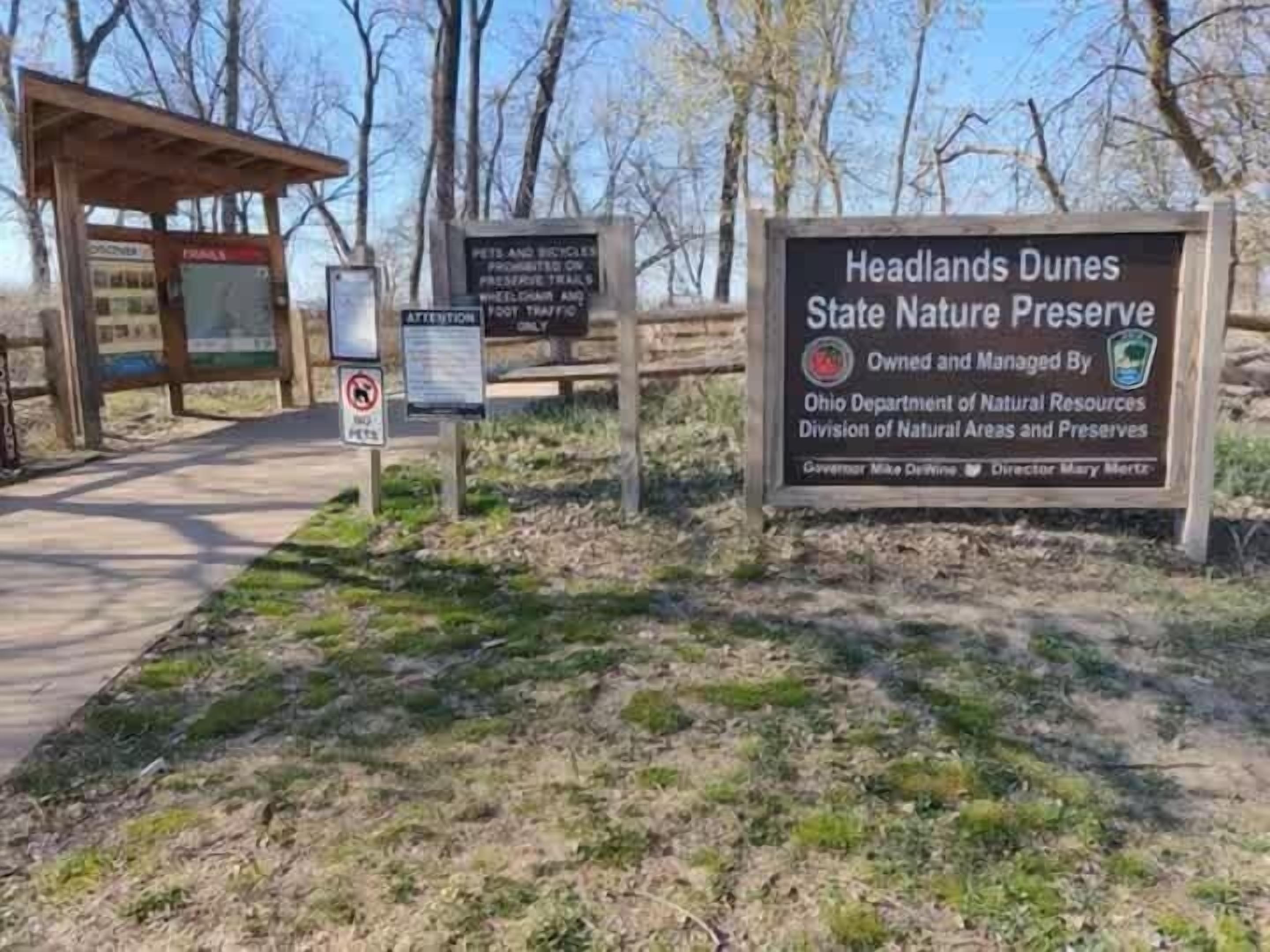 A sign for Headlands Dunes State Nature Preserve with a wooden structure in the background.