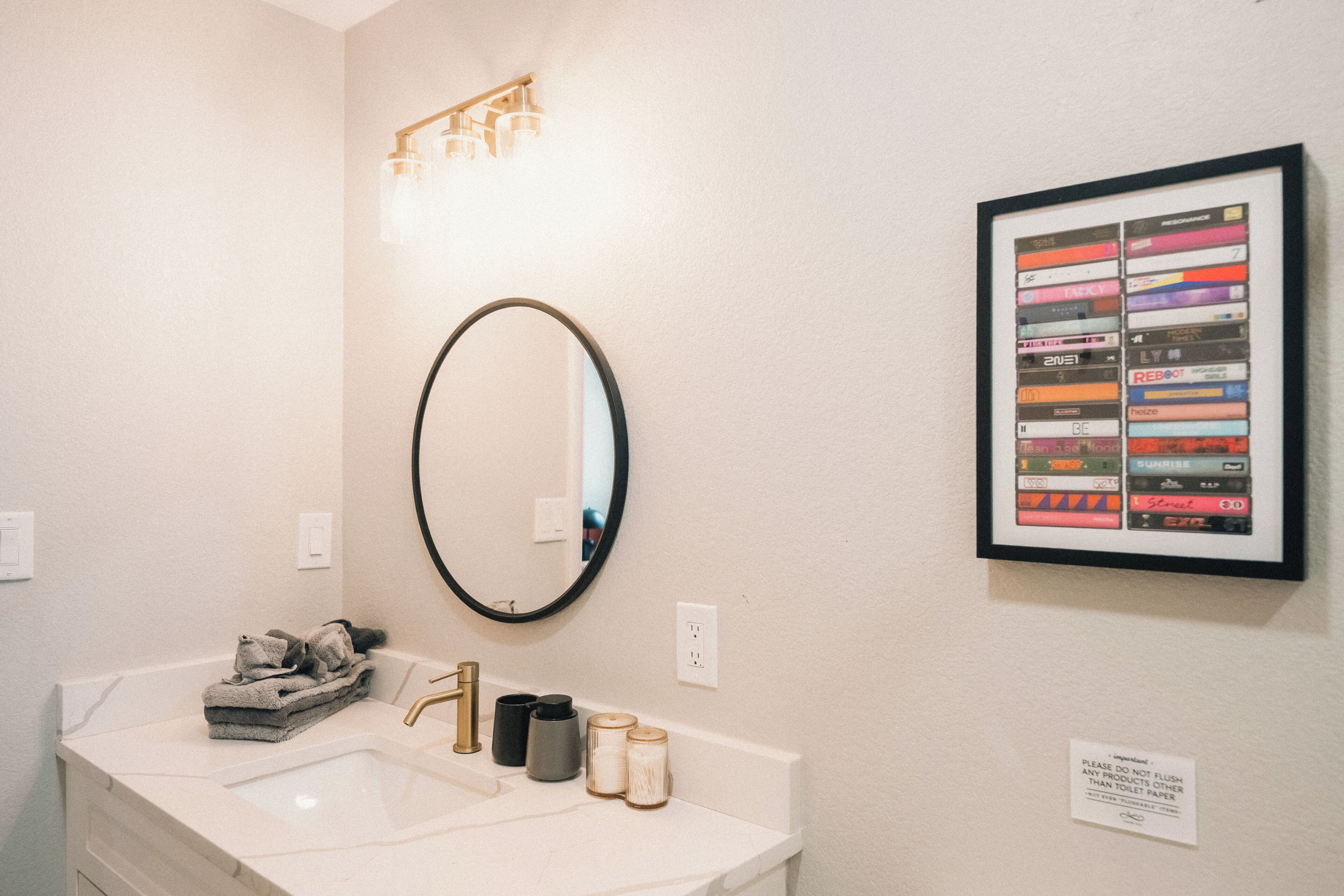 A bathroom with a sink, mirror, and framed music collection on the wall.