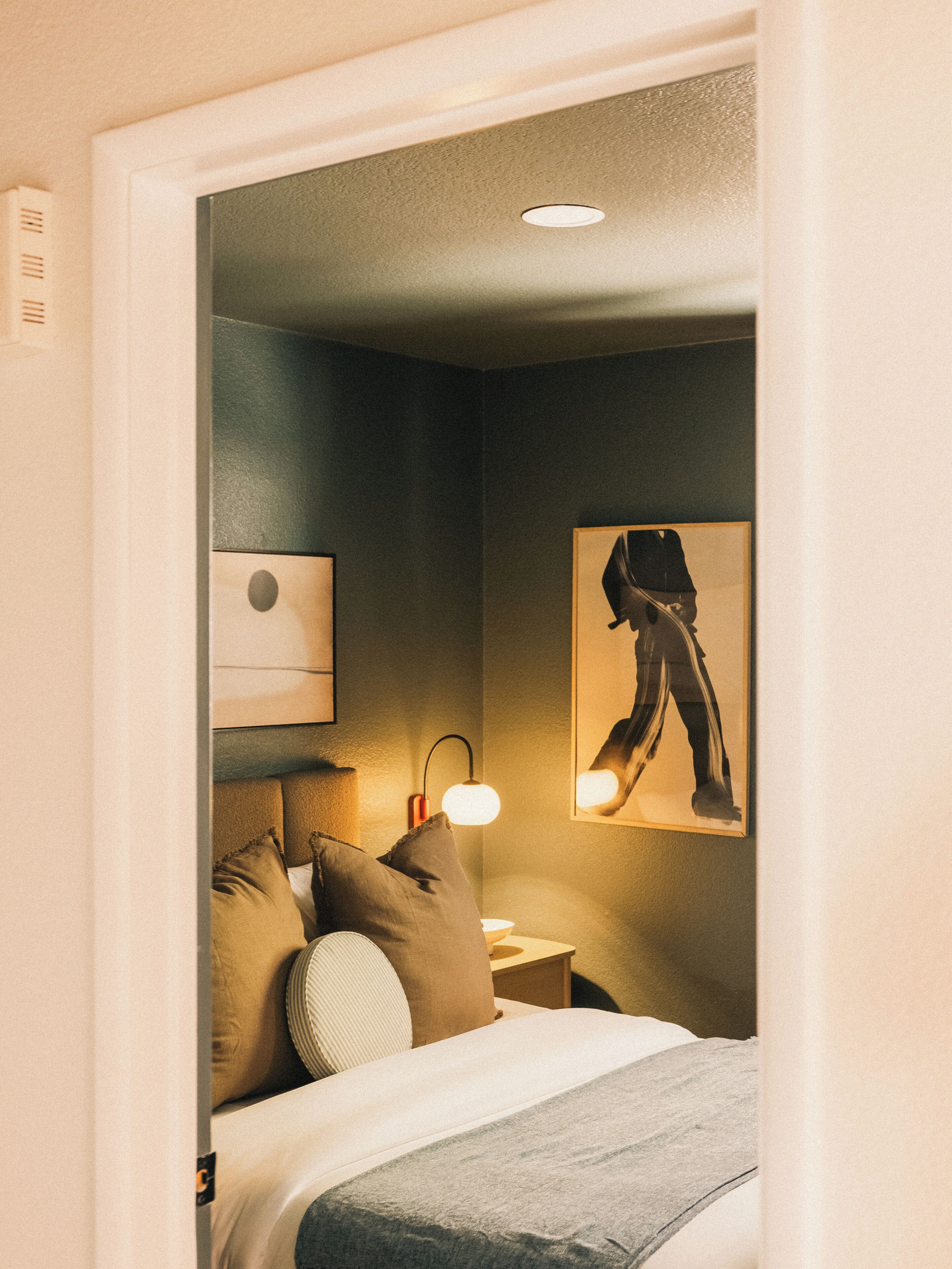 Une chambre d’hôtel avec un lit, des oreillers, une table de chevet, une lampe et un tableau encadré au mur.