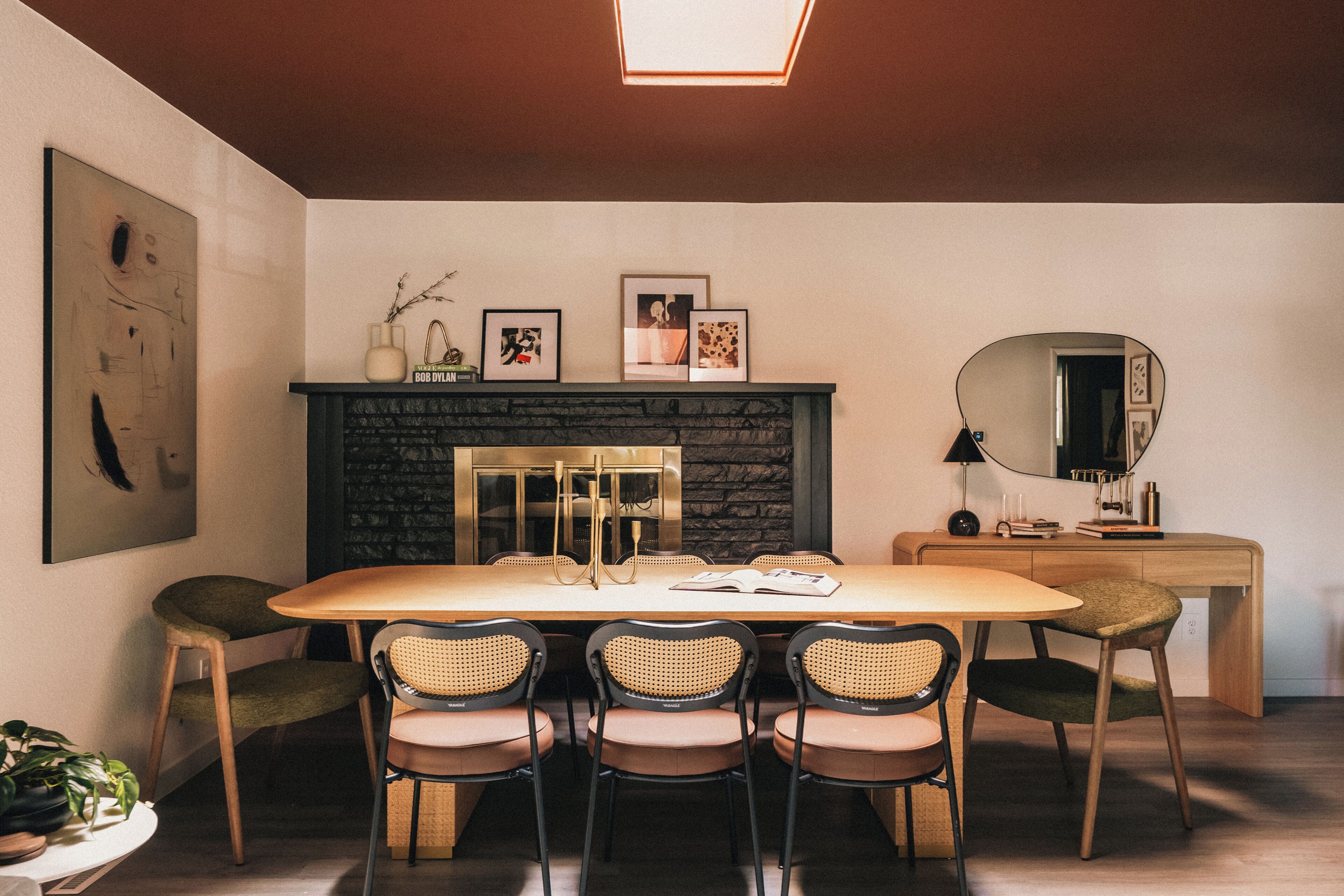 Un comedor con una mesa redonda, cuatro sillas, una chimenea, cuadros enmarcados y un espejo.