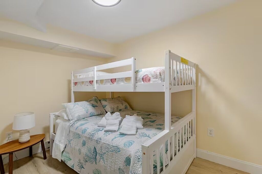 Een stapelbed met een bedovertrek met dessin, een nachtkastje met een lamp en een klein houten krukje.