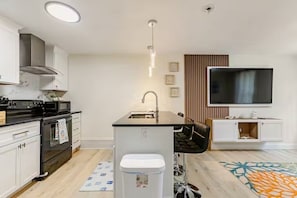 Moderni keittiö, jossa on keskeinen saareke, sisäänrakennettu uuni ja seinälle asennettu litteänäyttöinen televisio.