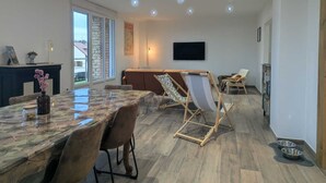 Een ruime woonkamer met een eettafel, stoelen, een bank, een televisie en een open haard.