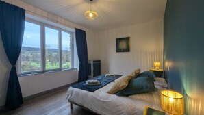 Een slaapkamer met een bed, een raam met gordijnen, een bedlampje en een aan de muur hangend schilderij.