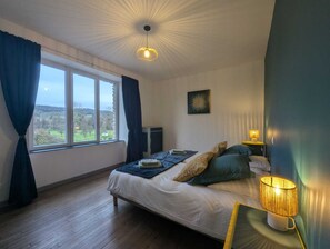 A bedroom with a bed, a window with curtains, a bedside lamp, and a wall-mounted picture. - Les Champs Dessus - Sarrey (Sarrey)