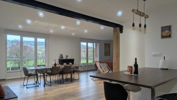 Ruime eethoek met een lange tafel en stoelen, grote ramen met uitzicht op groen, en een modern plafond met inbouwverlichting.