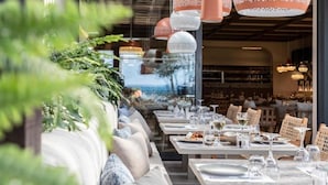 Un restaurante con terraza, mesas dispuestas con platos y vasos, y lámparas colgantes.