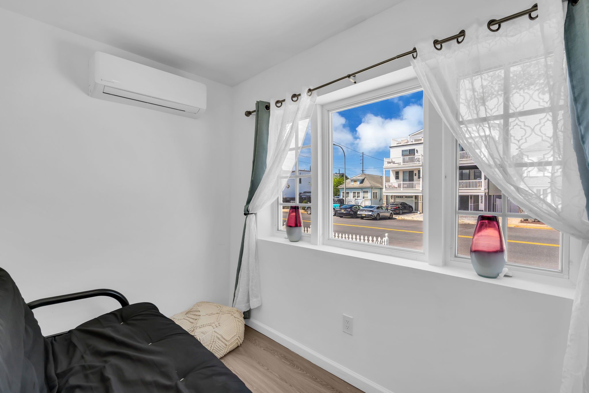 Una habitación con cama, ventana con cortinas, aire acondicionado y un florero en el alféizar.