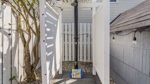 Un espacio exterior cubierto con una pérgola, una cerca blanca y una pequeña mesa con un adorno de playa.