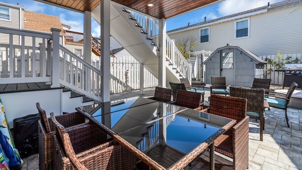 Un patio techado con una mesa de vidrio, sillas de mimbre, una escalera y una piscina.