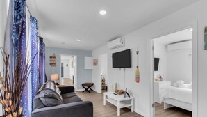 Una sala de estar moderna con un sofá gris, una mesa de centro blanca y un televisor de pantalla plana montado en la pared.
