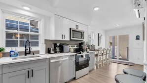 Una cocina moderna con armarios blancos, microondas, cafetera y lavavajillas.