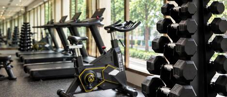 Un gimnasio con cintas de correr, bicicletas estáticas y un estante con mancuernas.