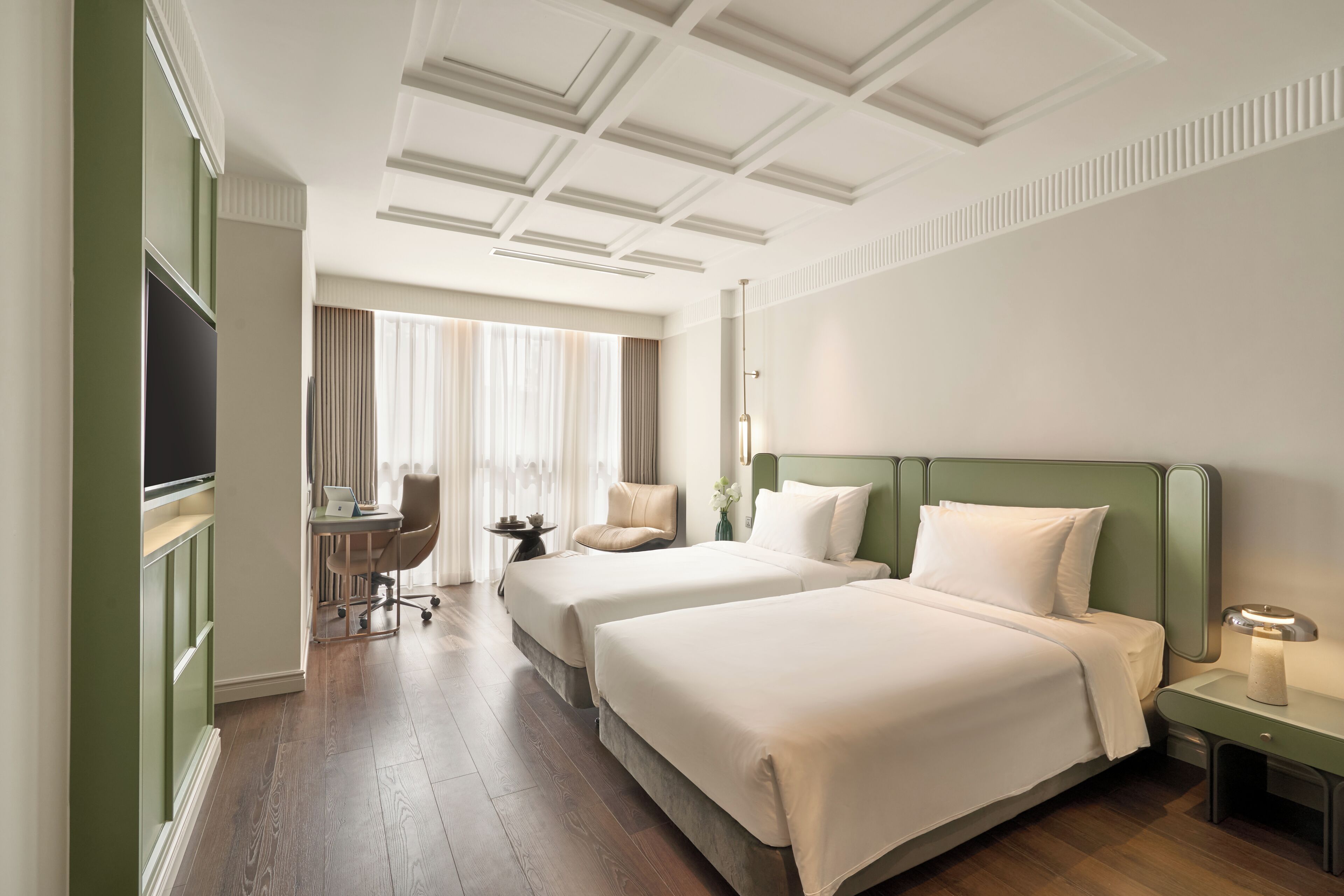 A hotel room with two beds, a desk, a chair, a TV, and a window with curtains.
