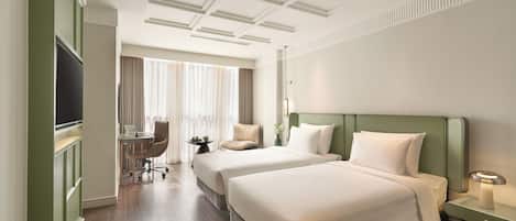 Habitación de hotel con dos camas, un escritorio, una silla, un televisor y una ventana con cortinas.