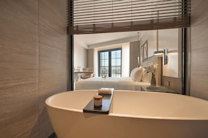 A modern bathroom with a freestanding bathtub, a glass shower enclosure, and a large window providing natural light.