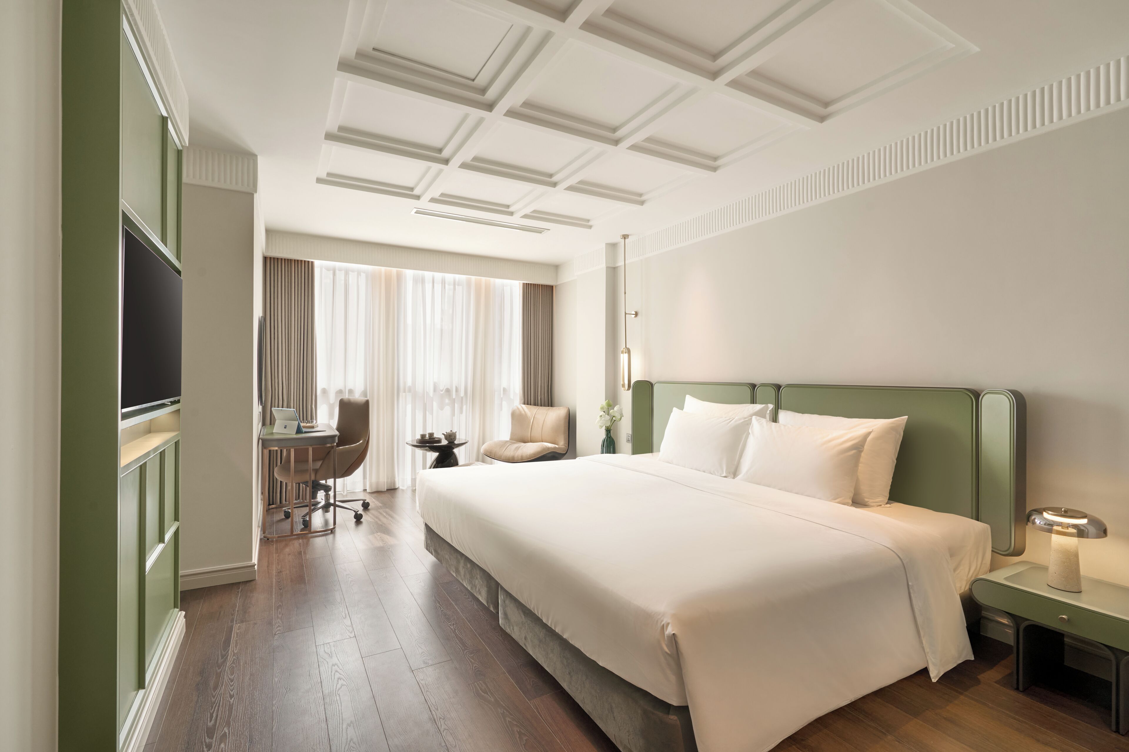 Habitación de hotel con una cama grande, un escritorio, una silla, un televisor y una mesita de noche con lámpara.