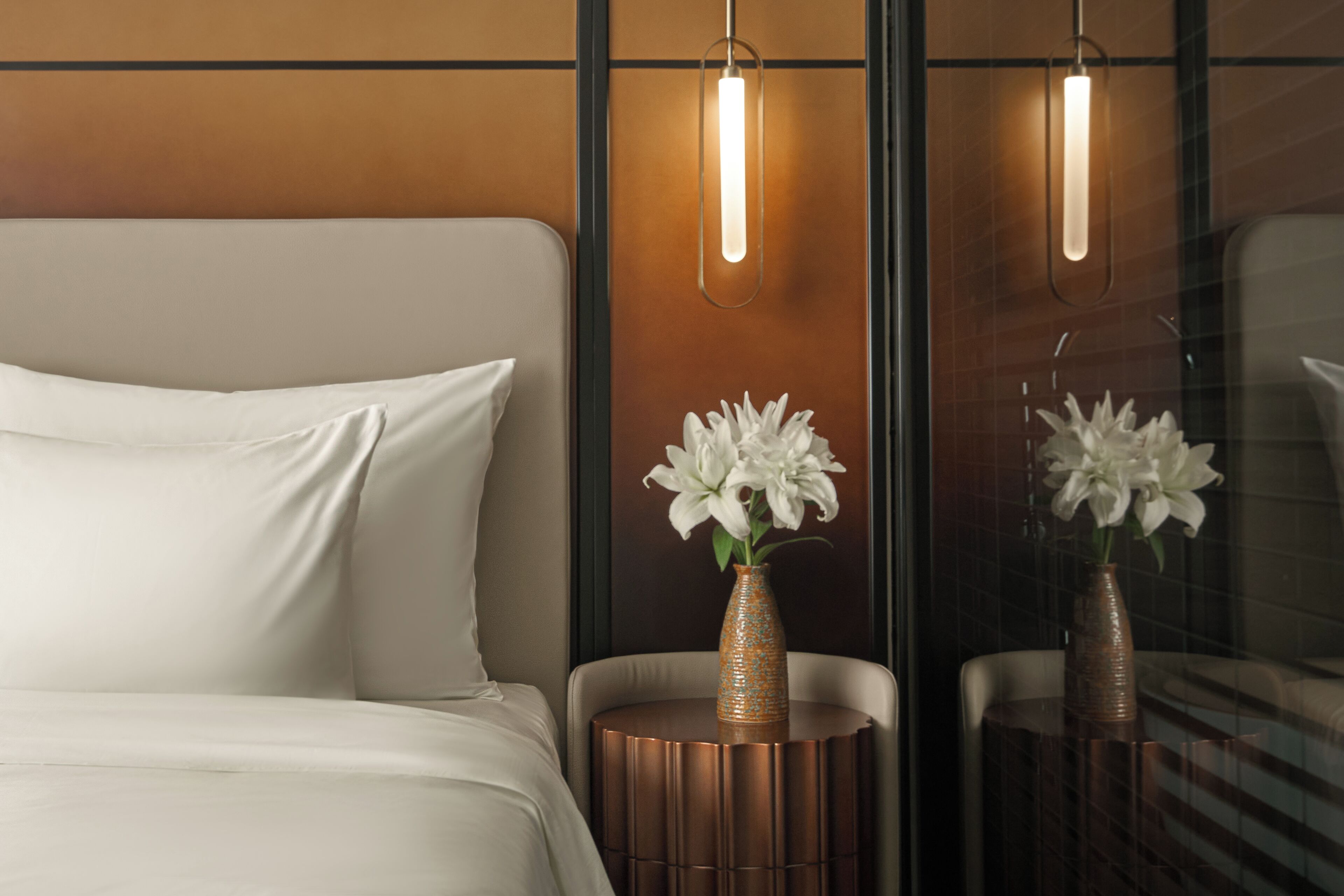 A modern hotel room with a bed, two side tables with vases, and a large mirror.