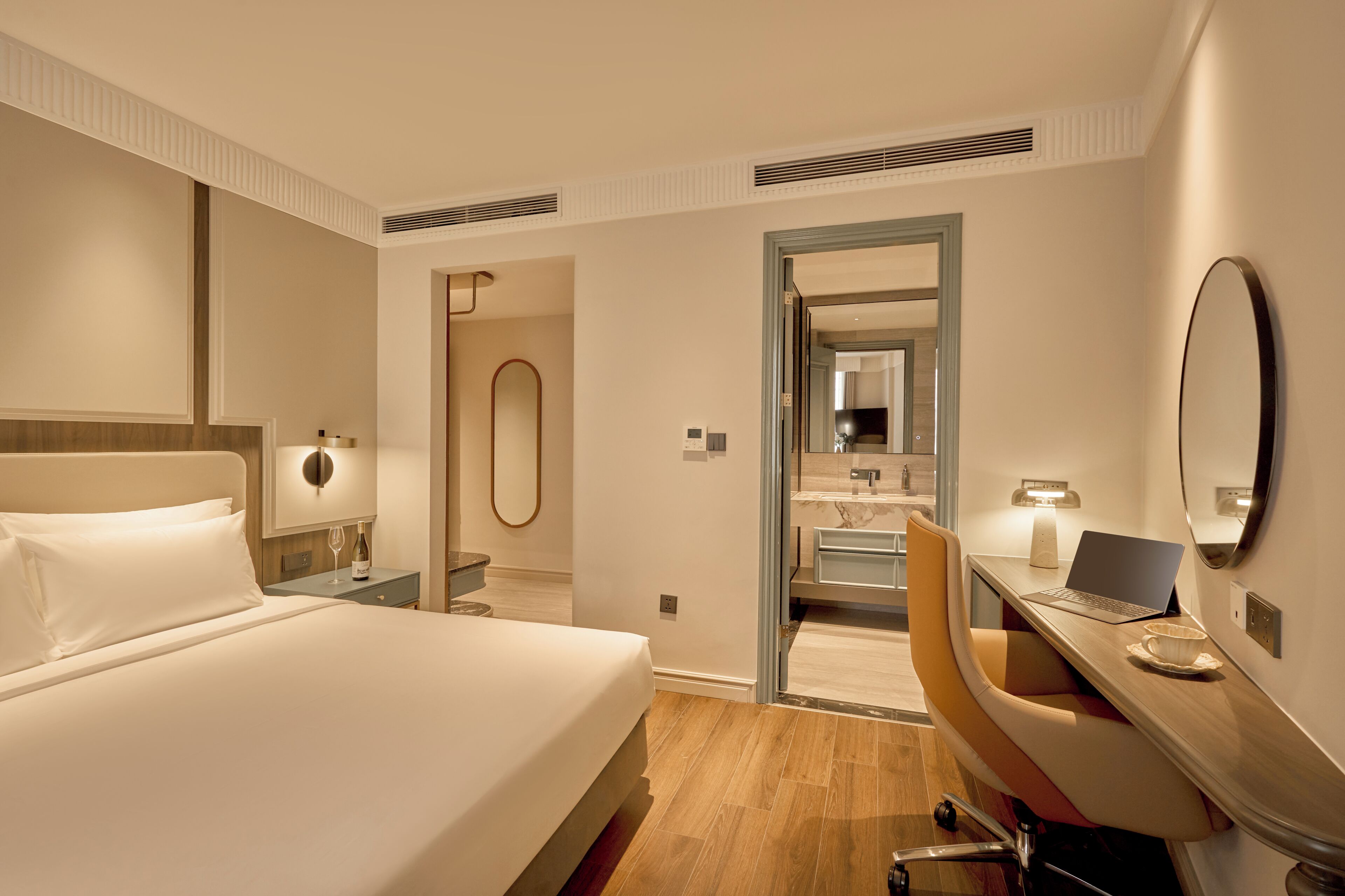 Habitación de hotel con cama, escritorio, silla y baño visible a través de una puerta abierta.