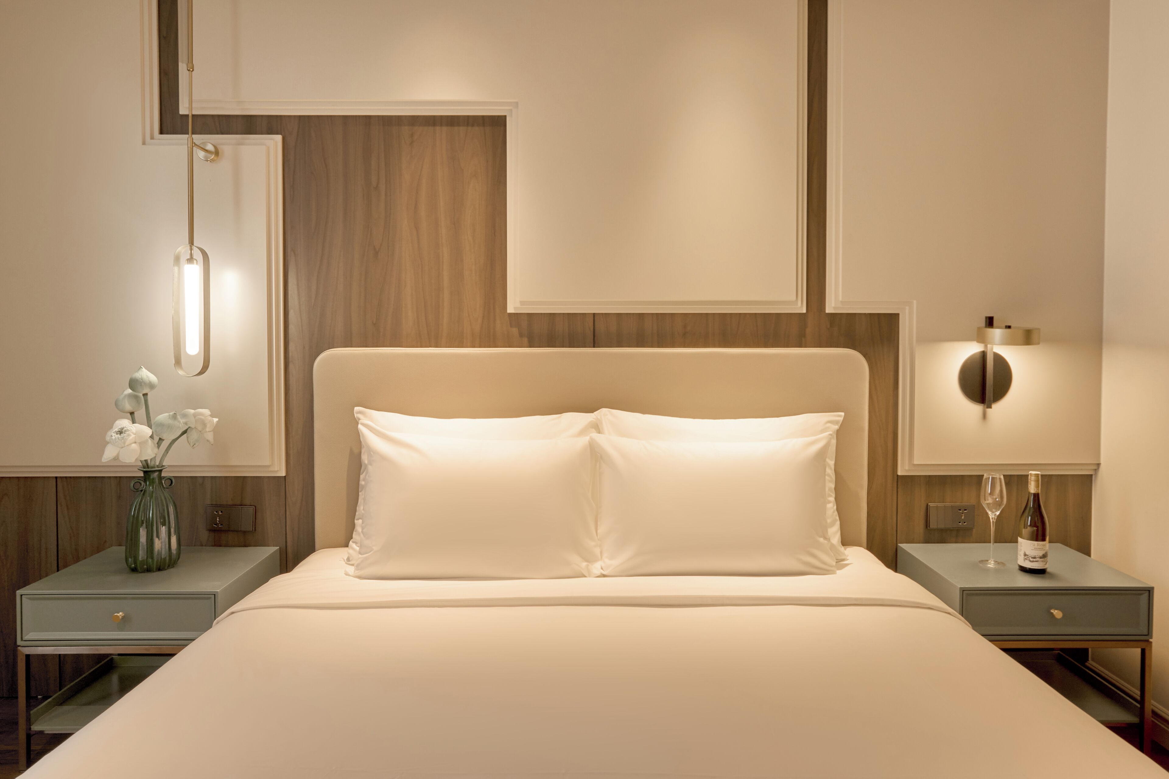 Een keurig ingerichte hotelkamer met een groot bed, nachtkastjes, een bloemenvaas en wandlampen.