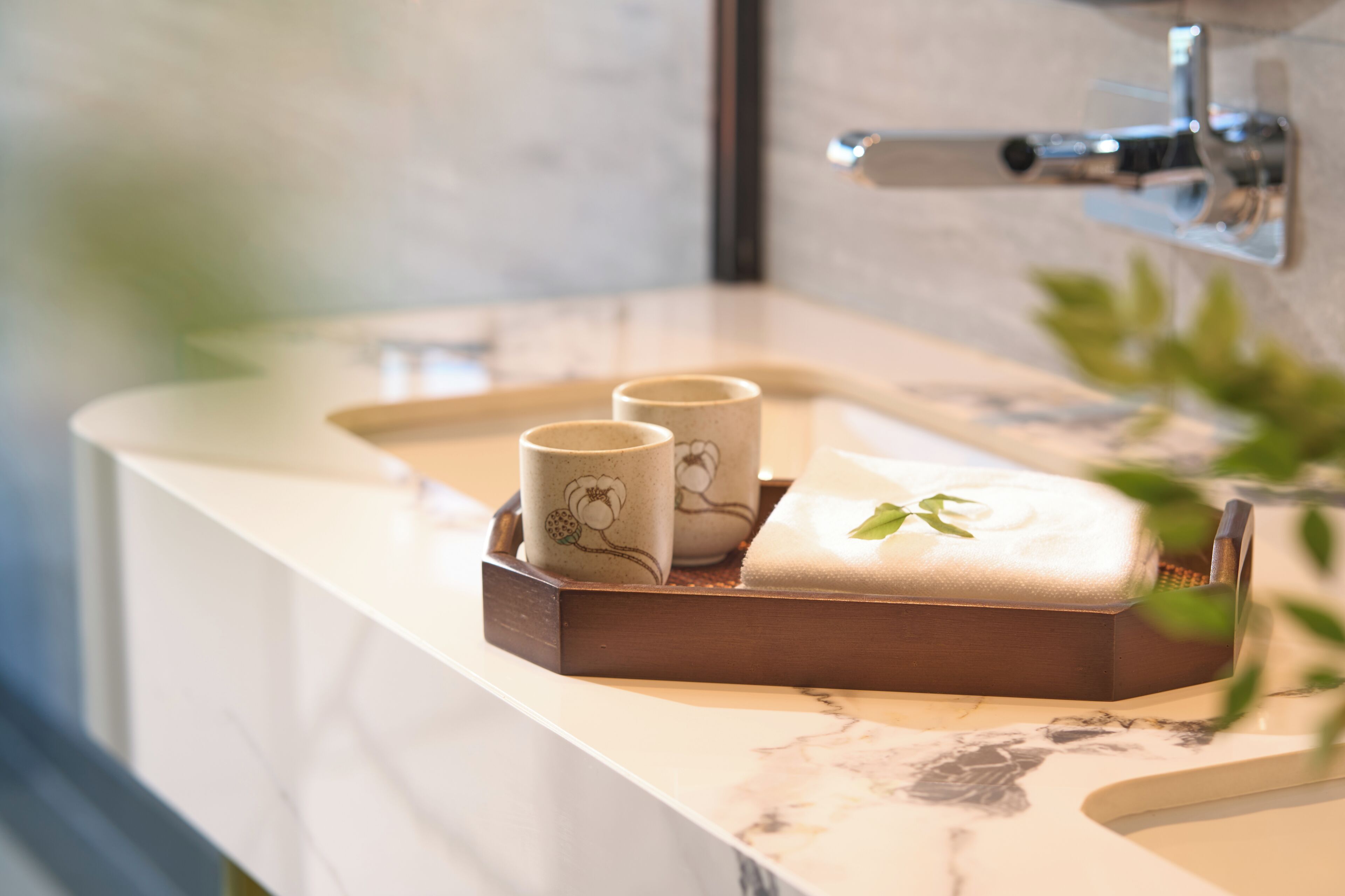 Une salle de bain avec un comptoir en marbre, un plateau sur lequel reposent deux tasses en céramique et une serviette.