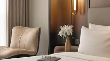 A hotel room with a bed, a chair, a vase with flowers, and a bedside table.