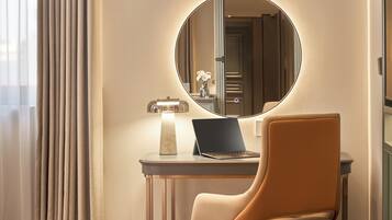 A room with a round mirror, a laptop on a small table, a chair, and a lamp.