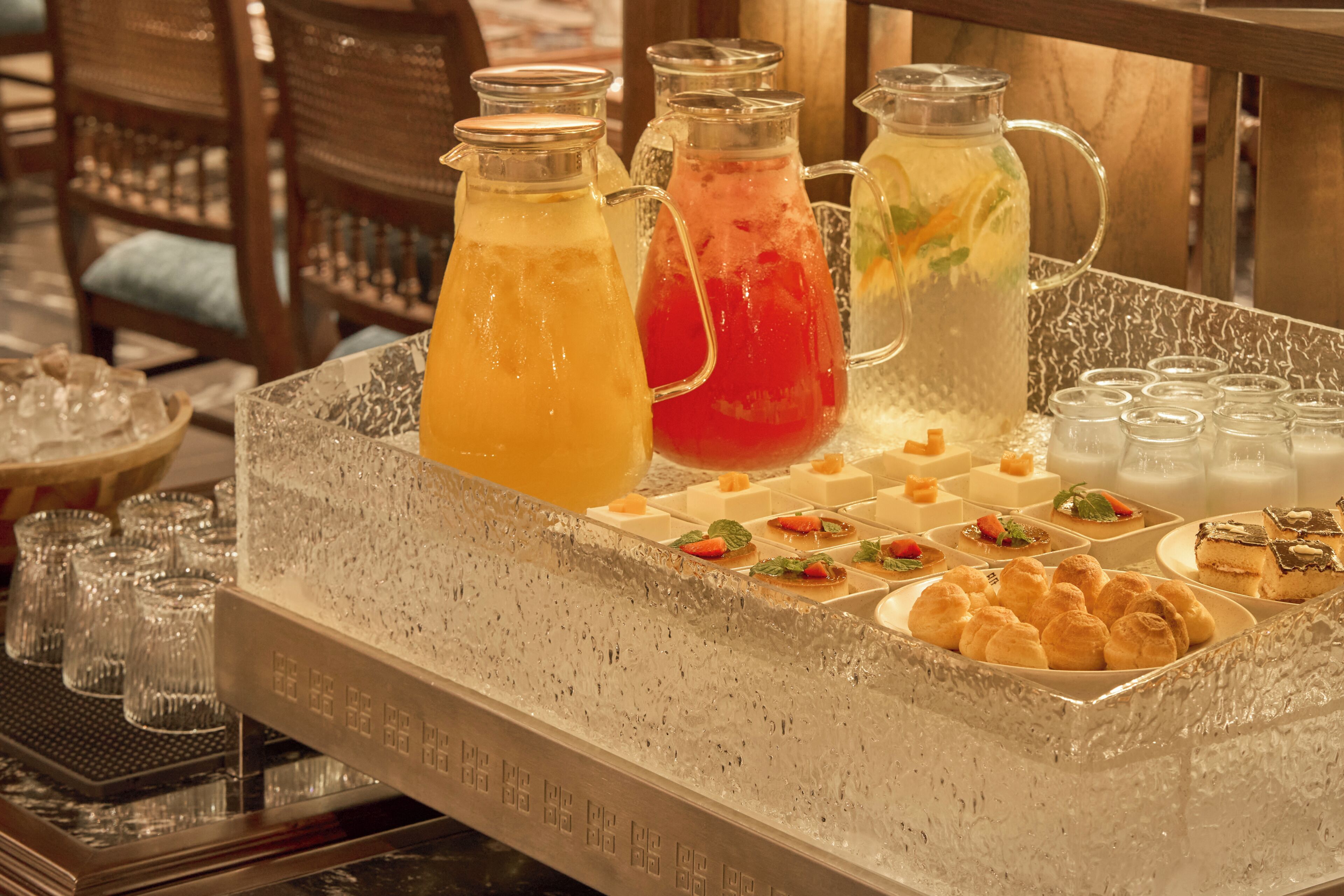 A buffet table with various beverages in pitchers and a selection of desserts.