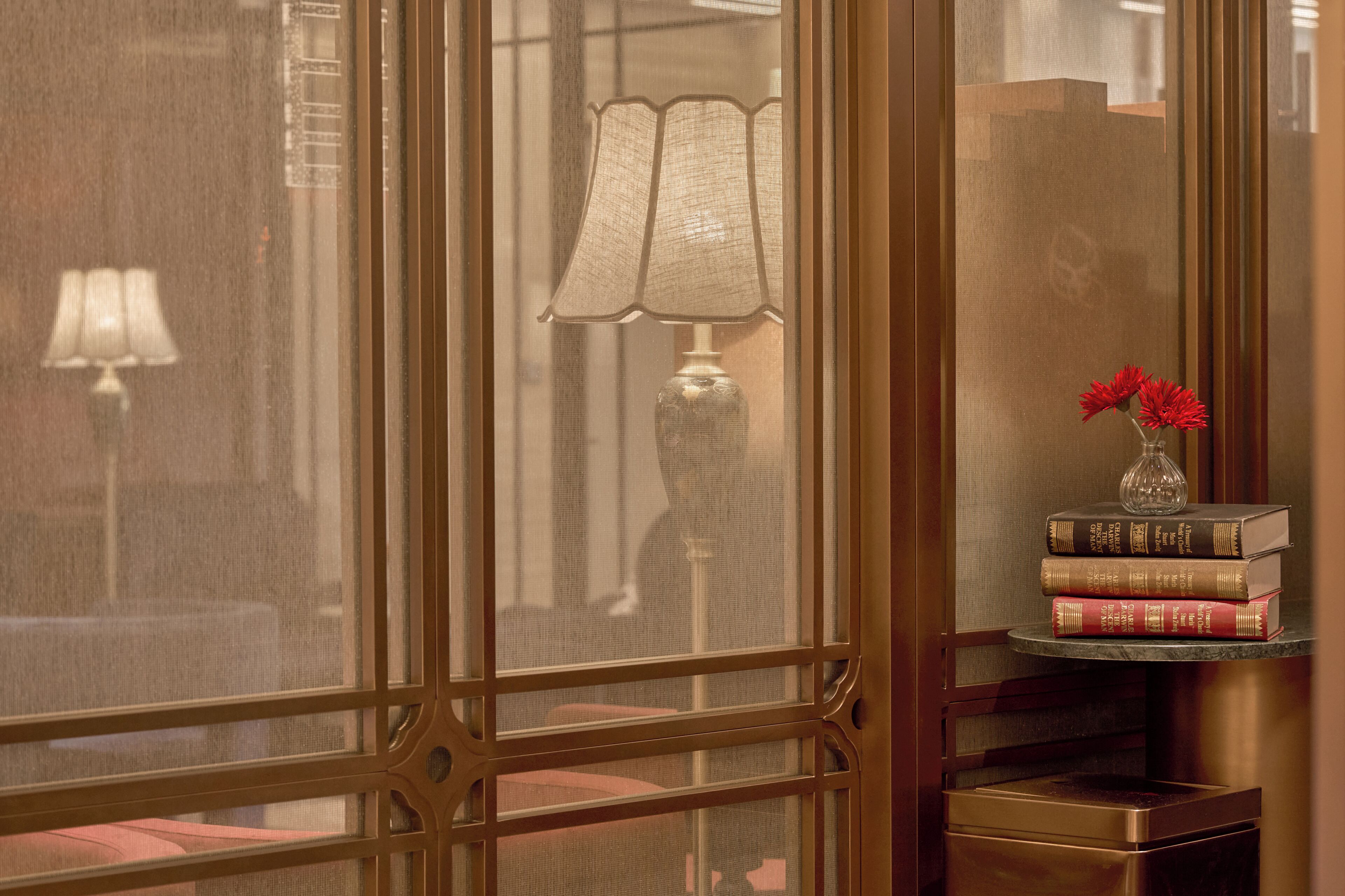 Une pièce avec une grande fenêtre, une lampe et une petite table sur laquelle se trouvent des livres et des fleurs.