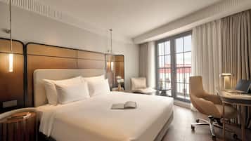 A hotel room with a large bed, a desk with a laptop, a chair, and a view of the outside through a window.