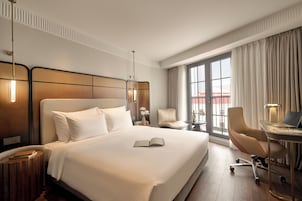 A hotel room with a large bed, a desk with a laptop, a chair, and a view of the outside through a window.