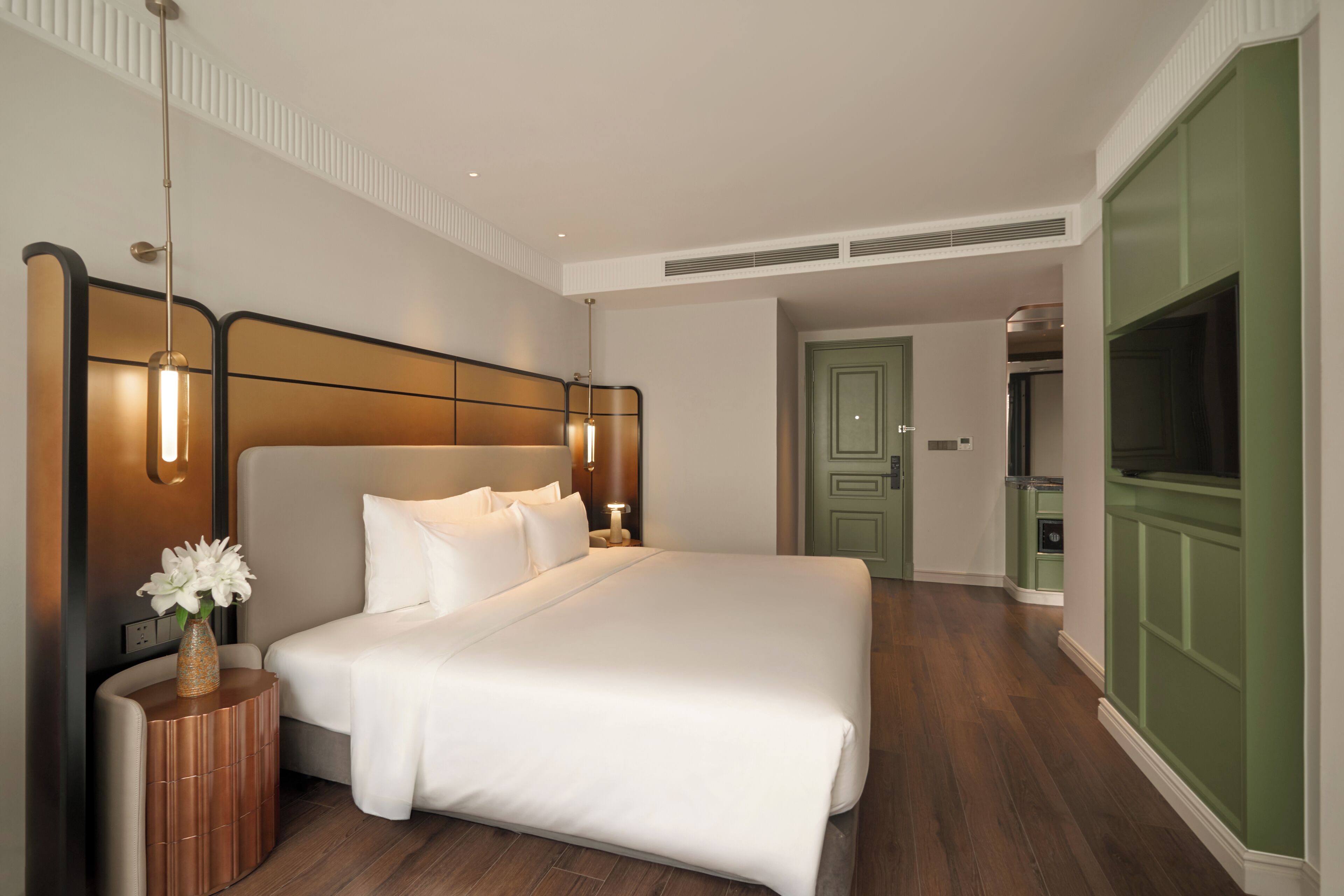 Ein Hotelzimmer mit einem großen Bett, Nachttischlampen, einem Nachttisch, einer Vase mit Blumen und einem Fernseher.