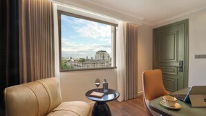 A hotel room with a view of the city, a sofa, a table with a laptop, a glass of wine, and a book. - Solaria d'Oriente Hotel (Hanoi)