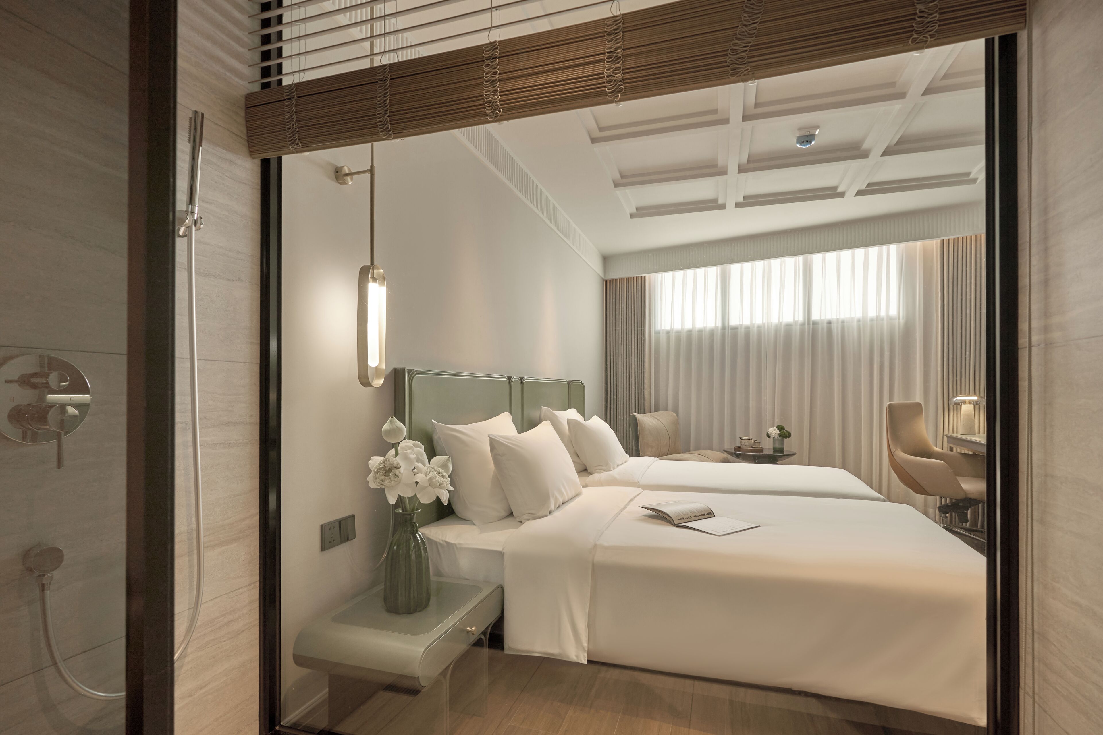 A hotel room with a large bed, a bedside table with a vase of flowers, a chair, and a desk with a lamp.
