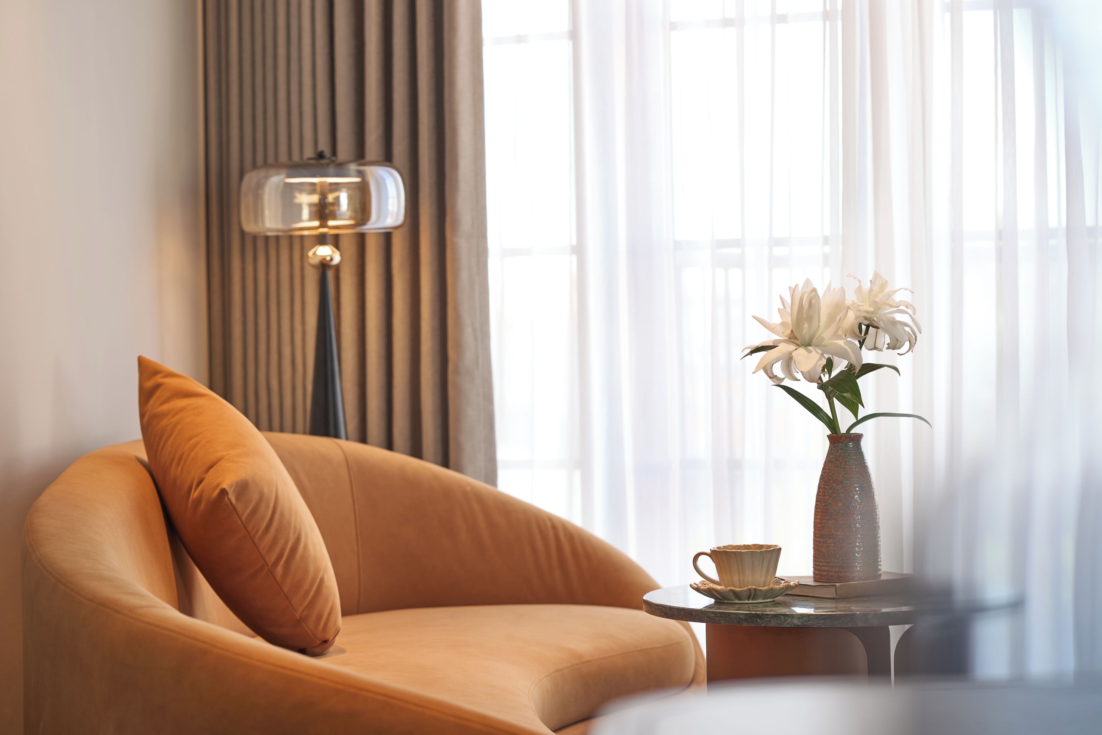 A room with a sofa, a lamp, a vase with flowers, and a table.