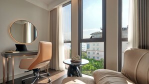 A modern hotel room with a large window, a round mirror, a desk with a laptop, a comfortable sofa, and a small table with a tray. - Solaria d'Oriente Hotel (Hanoi)