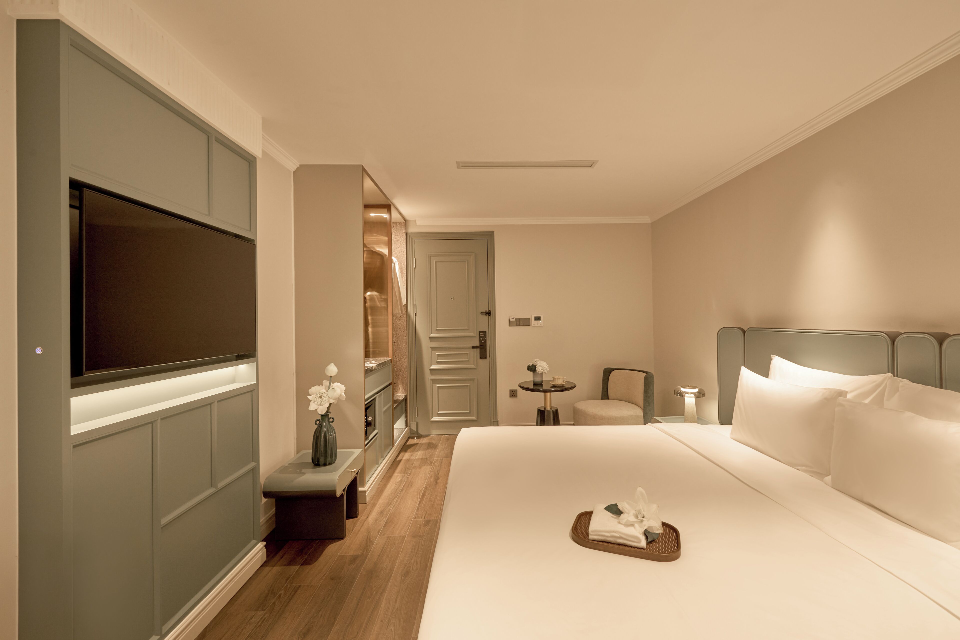 A hotel room with a large bed, a flat-screen TV, a small table with a vase, and a chair.