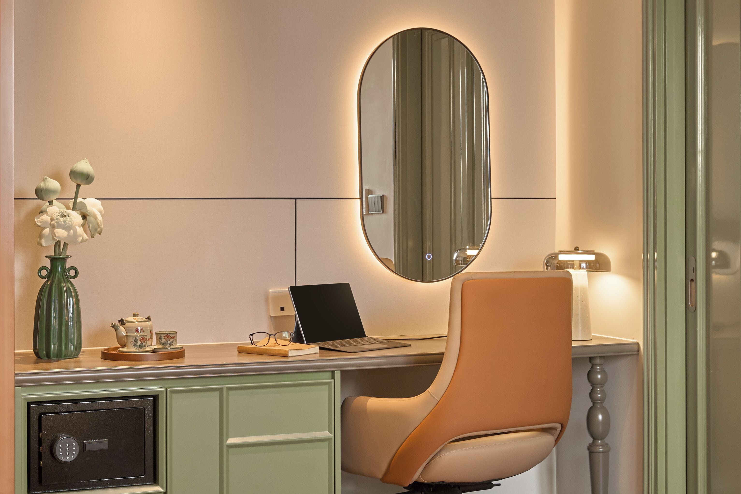 A room with a desk, chair, mirror, vase with flowers, and a safe.