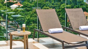 Two lounge chairs with towels, a glass of beer, and a small table on a balcony with a city view. - Solaria d'Oriente Hotel (Hanoi)