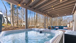 Un jacuzzi bajo una zona techada con vistas a árboles y un sofá con cojines.