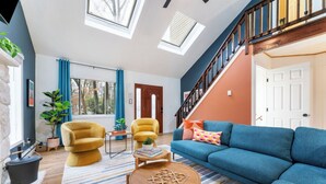 Una sala de estar moderna con un sofá azul, sillones amarillos, una mesa de centro de madera y una escalera con barandilla de madera.