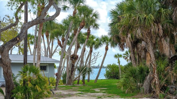 A pathway leading to a building surrounded by palm trees and a view of the water. - Coastal Retreat with Private Pool on Manasota Key (Englewood)
